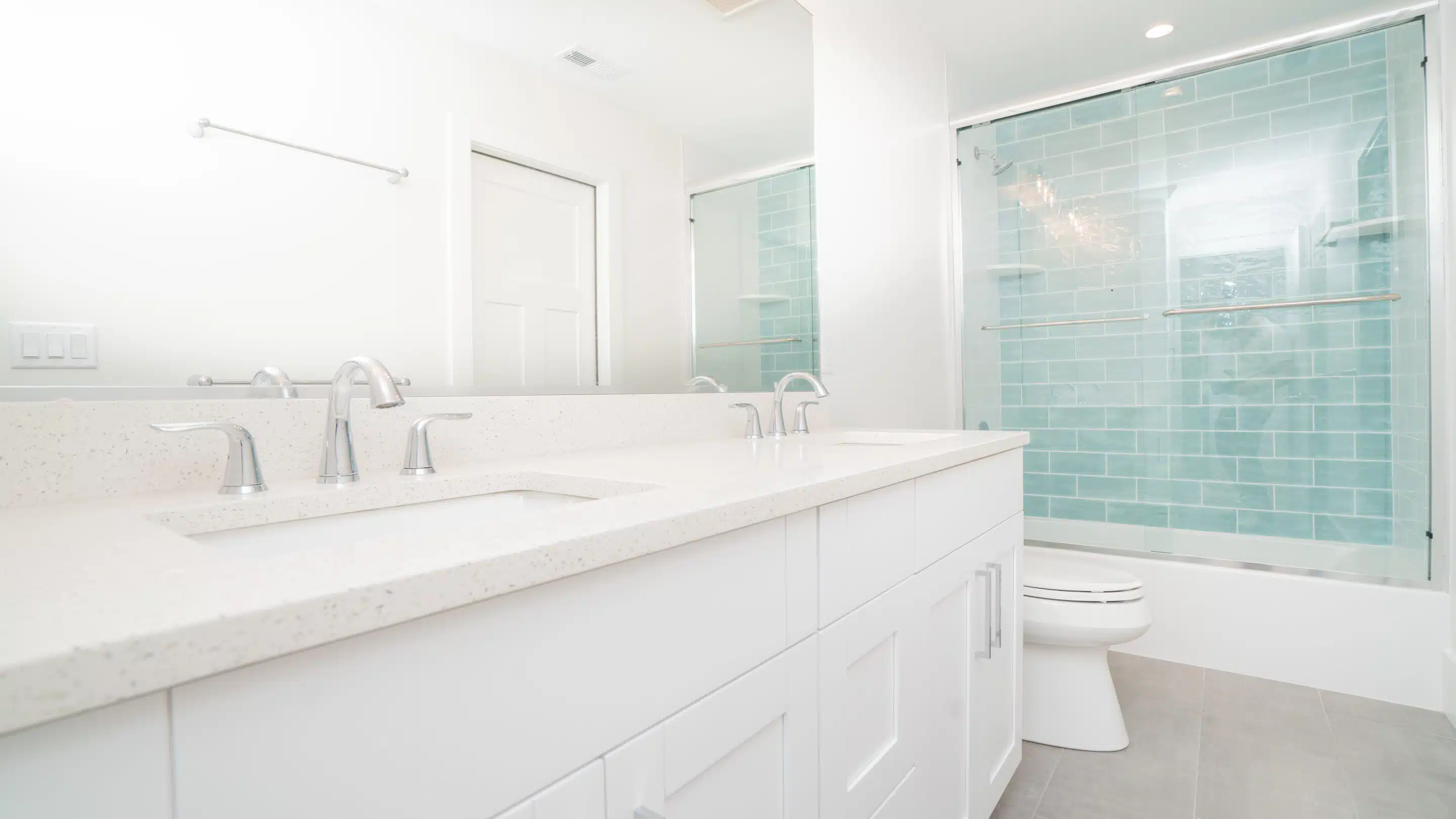 Modern white bathroom with double vanity and light blue subway tile shower.