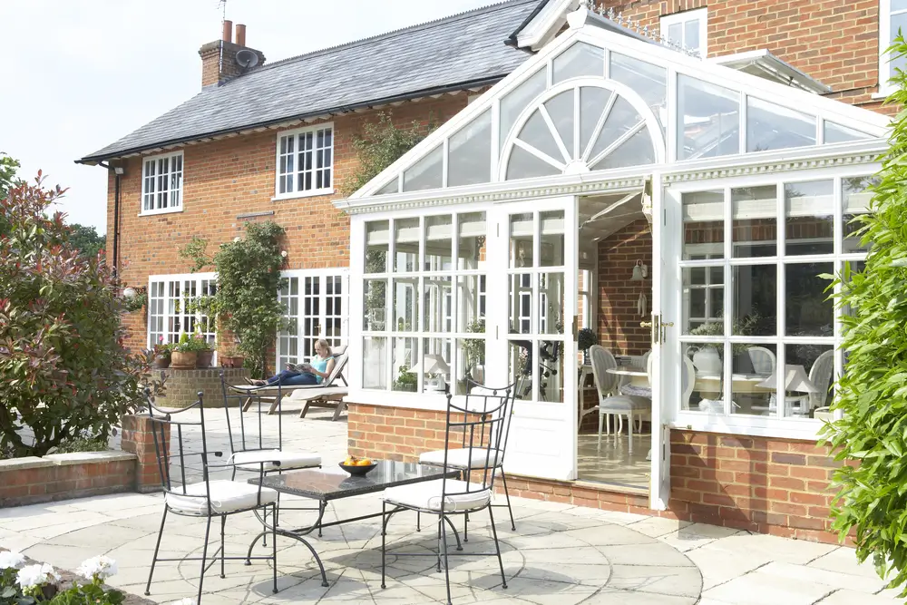 Attached brick and glass conservatory in-law suite featuring large windows and direct access to a paved outdoor patio.