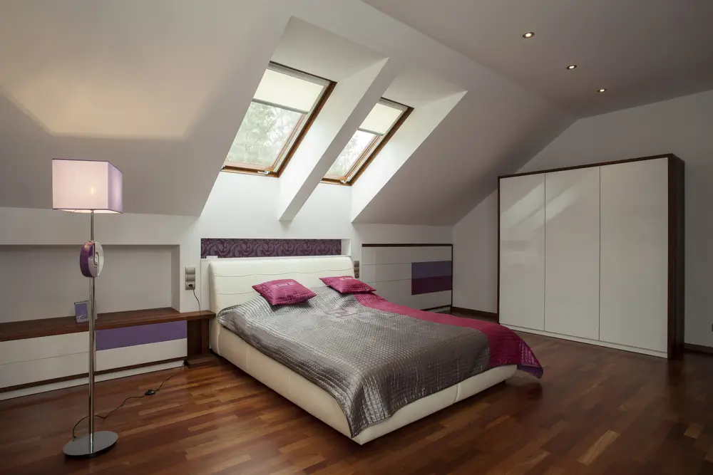 Modern attic in-law suite bedroom featuring sloped ceilings, dual roof skylights, rich hardwood floors, and fitted white wardrobes.