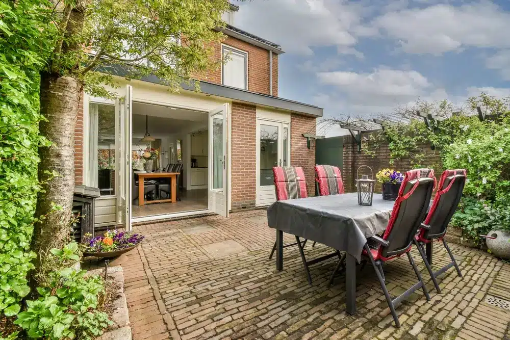 Exterior brick ground-floor attached addition with open French doors leading to a brick patio with dining table.