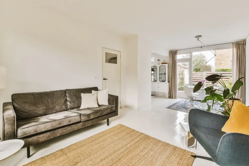 Modern bright in-law suite living room with white floors, comfortable seating, and an adjacent sunlit dining area with full glass doors.